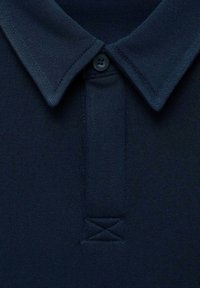 Námornícky modrá bavlnená polo tričko s klasickým golierom, ktoré má jediné zapínanie na gombík, rebrovanú textúru a šitý trojuholníkový akcent.