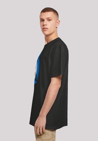 Schwarzes Baumwoll-T-Shirt mit lockerer Passform, das ein blaues Grafikdesign auf der Vorderseite zeigt. Kurze Ärmel und runder Ausschnitt.