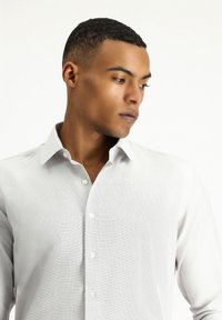 Camisa blanca de botones con tejido texturizado, cuello clásico y seis botones, exhibida en un modelo con pelo corto y una expresión neutral.