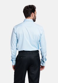 Lichtblauw overhemd met lange mouwen en een standaardkraag, gecombineerd met zwarte broek met achterzakken en knoopaccenten.