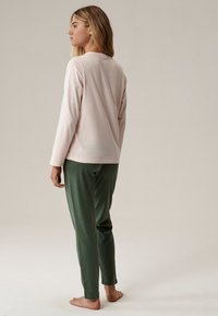 Długi rękaw jasnoróżowa bluzka w zestawieniu z zielonymi spodniami dresowymi. Miękki materiał, luźny krój, gładka faktura, bez widocznych wzorów czy metalowych elementów.