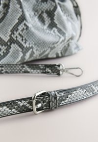 Sac à main imprimé serpent gris et blanc avec une finition texturée. Comprend une bandoulière amovible et une quincaillerie argentée, y compris une boucle et un clip.
