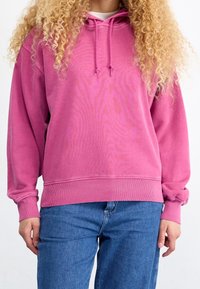 Felpa rosa con cappuccio, caratterizzata da una vestibilità rilassata, polsini e orlo a costine. Realizzata in un morbido tessuto con una sottile trama. Abbinata a jeans blu.