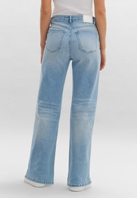 Lichtblauwe denim wijde broek met hoge taille, vijf zakken en subtiele vervaging, voorzien van een wit label op de achterkant van de tailleband.