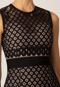 Robe noire avec une superposition texturée et transparente présentant un motif géométrique. Ceinture noire unie et design sans manches.