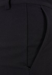 Nahaufnahme von schwarzen Stoffhosen mit einer Seitentasche und einem Bund mit detaillierten Nähten.