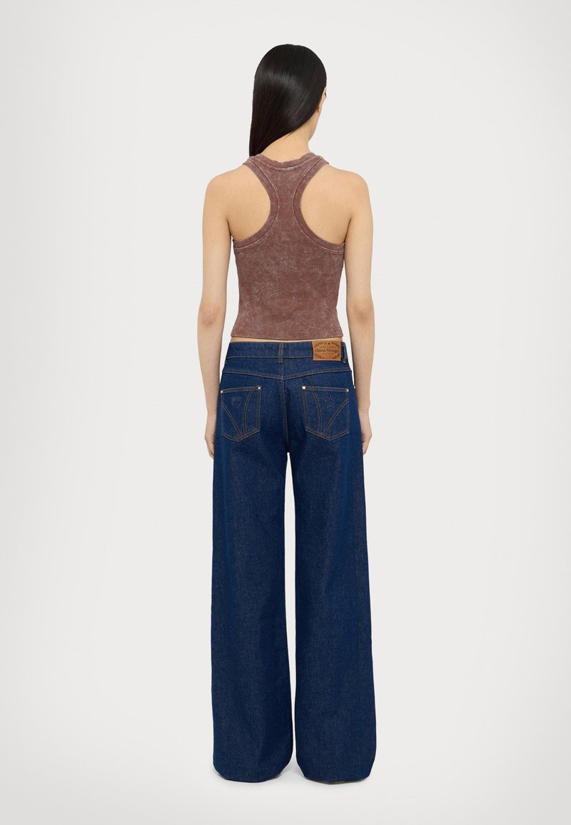 Un débardeur marron à côtes associé à un jean large bleu foncé. Les caractéristiques notables incluent un tissu texturé et un patch en cuir avec logo sur le jean.