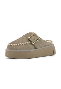 Chaussure slip-on en suede beige avec des coutures décoratives, une sangle à boucle et une semelle plateforme épaisse beige. Texture lisse avec un design à bout arrondi.
