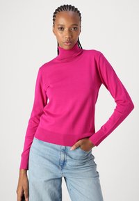 Fitted coltrui in felroze, gemaakt van zachte gebreide stof, met geribbelde mouwen en tailleband, gecombineerd met lichtblauwe relaxte jeans.
