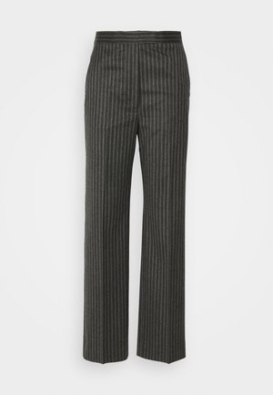 Persona vestida con un abrigo largo oscuro, pantalones anchos de rayas grises, suéter de cuello alto brillante y zapatos negros de tacón cuadrado con tiras en el tobillo.