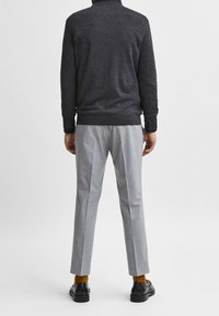 Mörkgrå tröja, ljusgrå byxor, senapsgula strumpor och svarta skor. Tröjan har ribbade manschetter och nederkant; byxorna är slim-fit med pressvecka.