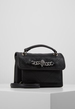 Sac à main en cuir noir avec motif matelassé, poignée supérieure, chaîne argentée et détail de fermoir en forme de main sur une surface blanche.