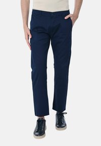 Pantaloni in cotone blu navy con vestibilità dritta, dotati di tasche laterali e passanti per cintura, abbinati a sneakers nere e una camicia aderente beige.