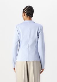 Ljusblå skräddarsydd kavaj med långa ärmar, notch-krage och strukturerade sömmar. Kombinerad med ljusgrå vida byxor.