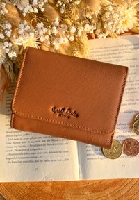 Brown leather wallet with a smooth texture, embossed logo, and decorative stitching, placed on open book pages and surrounded by coins.