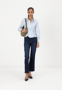 Blåstripet skjorte med knapper, mørke flagrende jeans, svarte lakksko med høye hæler, og en liten olivengrønn crossover-veske. Glatt stoff og tettsittende design.