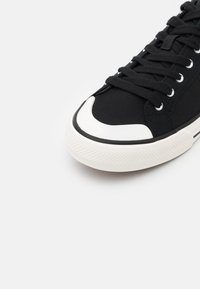 Baskets en toile noire avec bout rond, embout en caoutchouc blanc et semelle texturée ; dotées de lacets noirs et d'œillets argentés pour un ajustement sûr.