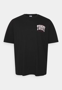 Camiseta de algodón negra con mangas cortas que presenta un logo blanco y rojo de "TOMMY" en el área del pecho izquierdo. Diseño simple de cuello redondo.