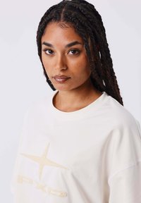 T-shirt oversize crema con scollatura rotonda. Presenta un logo testurizzato e un design a stella in una tonalità più chiara sul davanti. Tessuto morbido.
