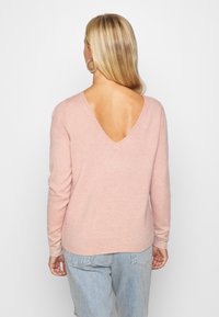 Helles rosa, langärmliges Sweater mit V-Ausschnitt auf der Rückseite, weichem Griff, gerippten Bündchen und Saum, kombiniert mit hellblauen Jeans.