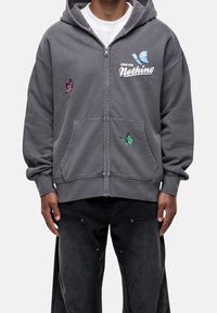 Sudadera gris con cremallera y bolsillo tipo canguro, con diseños de mariposas multicolores y el texto "GOOD FOR Nothing" en blanco.