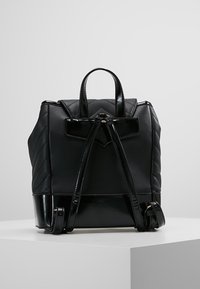 Mustat nahkareput, joissa on tikatut sivut, sileä pohja, säädettävät olkahihnat ja yläkahva, aseteltuna valkoiselle jalustalle.