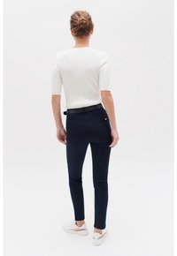 Pantalones ajustados en azul marino con una tela texturizada y dos bolsillos traseros, llevados con una camiseta blanca de corte entallado y zapatillas blancas.
