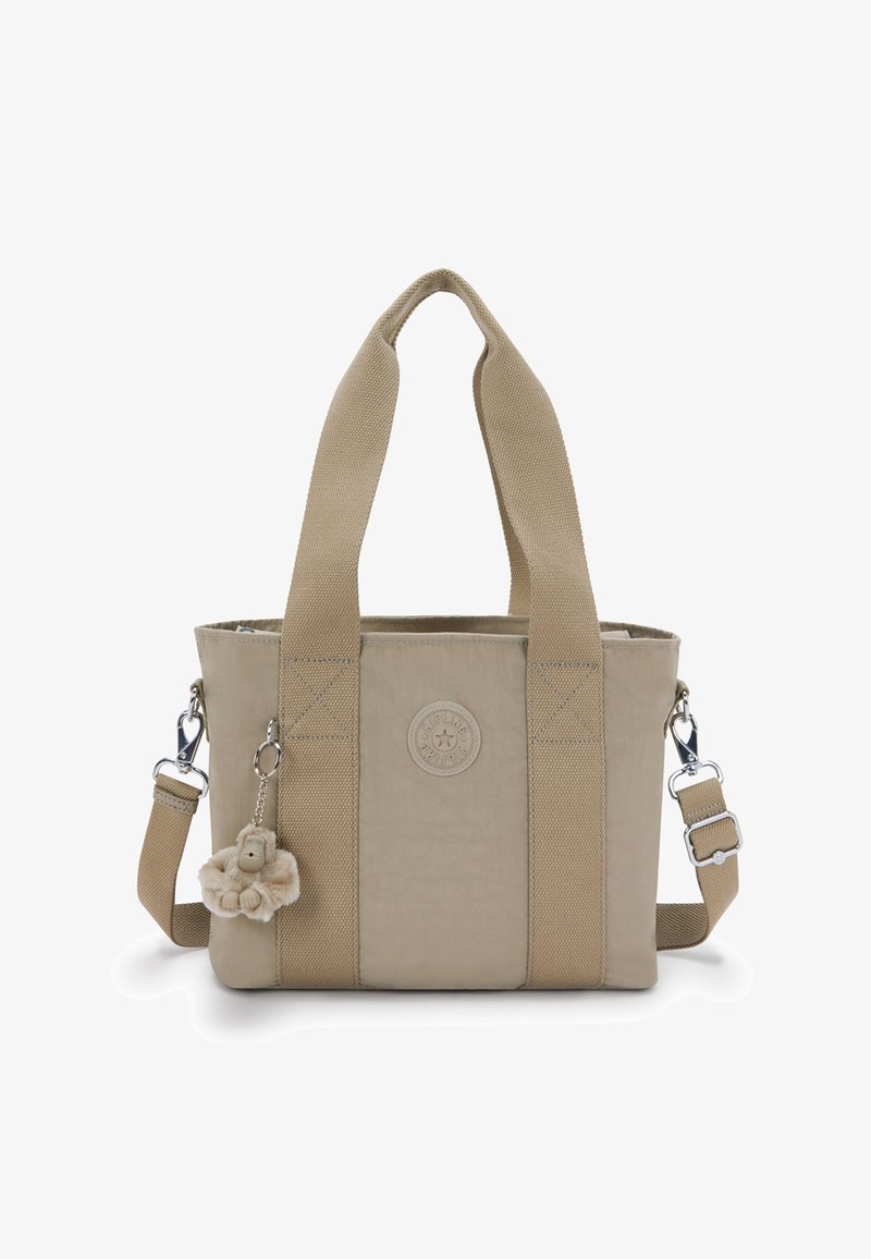 Sac cabas beige avec des anses larges en tissu, une bandoulière amovible, un écusson logo à l'avant, et un porte-clés peluche singe attaché.