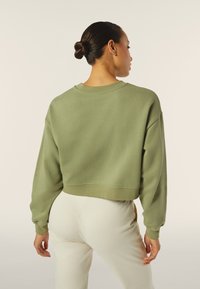 Sudadera verde corta con mangas largas, cuello redondo y una textura suave, combinada con pantalones ajustados de color claro.