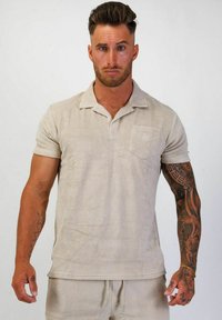 Beige kortärmad polo skorta i mjukt, strukturerat tyg med krage och en ficka på bröstet. Har en diskret logotyp på fickan.