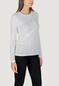 Camicia bianca a maniche lunghe con scollatura rotonda e una sottile grafica grigia sul petto. Realizzata in tessuto morbido, presenta una vestibilità slim.