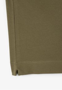 Olivgrön polotröja med texturerad stickad tyg, korta ärmar, sidoklyftor vid fållen och förstärkta sömmar.