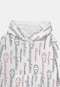 Biała bluza z kapturem z powtarzającym się logo Champion w kolorze czerwonym i granatowym, z regulowanym kapturem i przednią kieszenią typu kangur. Miękka tekstura materiału.