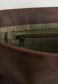 Lähikuva ruskean nahkalaukun sisäosasta, jossa näkyy vihreä kangasvetoketjullinen tasku, jossa on metallinen vetoketjun vetolaite.