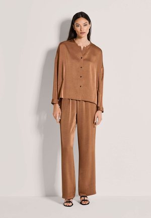 Bruin satijnen tweedelig set bestaande uit een kort gebuttoned top met een losse pasvorm en wijde broekspijpen, gecombineerd met zwarte sandalen met bandjes.