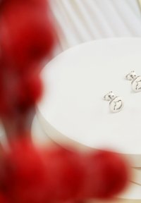 Srebrne kolczyki w kształcie okręgu z minimalistycznym wzornictwem i wygrawerowanym wzorem, wystawione na białej okrągłej platformie.