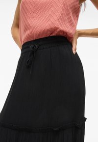 Haut texturé rose clair avec un motif en chevrons, associé à une jupe maxi plissée noire avec une taille à cordon de serrage et un ourlet volanté.