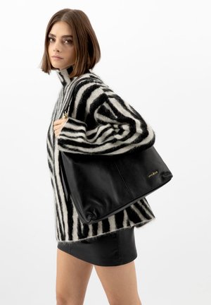 Jonge vrouw die een zwart-wit gestreepte trui en een zwarte rok draagt, met een grote zwarte leren handtas over haar schouder.