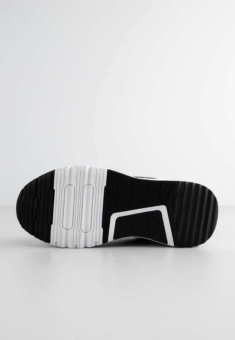 Suela de zapatilla deportiva en blanco y negro con goma texturizada, que presenta dibujos de tacos circulares y rectangulares, además de un diseño suave en blanco.