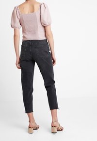 Blusa rosa chiaro con maniche a sbuffo e schiena quadrata, abbinata a jeans scuri a vita alta e sandali beige con tacco, che mostrano una vestibilità comoda.