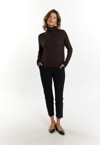 Brauner Rollkragenpullover mit langen Ärmeln, kombiniert mit schwarzen, eng anliegenden Hosen und schwarzen Ballettschuhen. Einfaches, elegantes Design mit glatter Textur.
