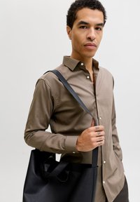 Καφέ πουκάμισο με κουμπιά, μακριά μανίκια, με μαύρη δερμάτινη τσάντα ώμου με απαλή υφή και διασταυρούμενα λουριά. Μινιμαλιστικός σχεδιασμός, ουδέτερα χρώματα.