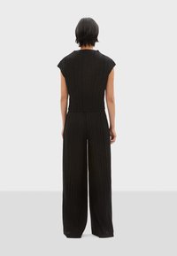 Zwarte ribbel jumpsuit met kapmouwen, aangesloten lijfje en wijde broekspijpen, met een textuurstof en een naadloos rugontwerp.
