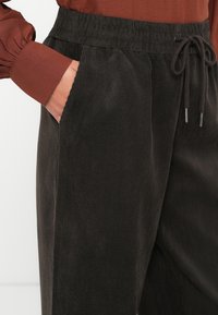 Tumed kortsukangast püksid pehme tekstuuriga, elastse pusaga, nööriga ja küljetaskutega. Värv on sügav tumehall.