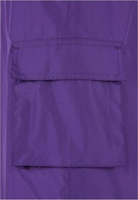 Lila Stoff mit strukturierter Oberfläche, mit einer rechteckigen aufgenähten Tasche auf der Vorderseite. Einfaches Design, keine sichtbaren Beschläge.