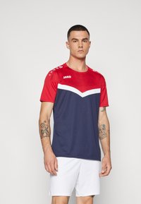 Rode en marineblauwe korte mouwen jersey met witte chevron details; heeft textuur op de schouders en een logo. Gedragen met witte shorts.