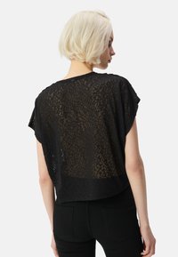 Top corto negro hecho de material transparente con un estampado de leopardo, que presenta mangas cortas sueltas y un ajuste relajado.
