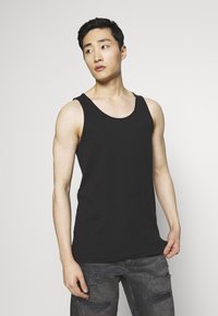 Top in cotone nero senza maniche con scollo tondo e spalline larghe, abbinato a jeans grigi strappati. Tessuto liscio, design minimal.