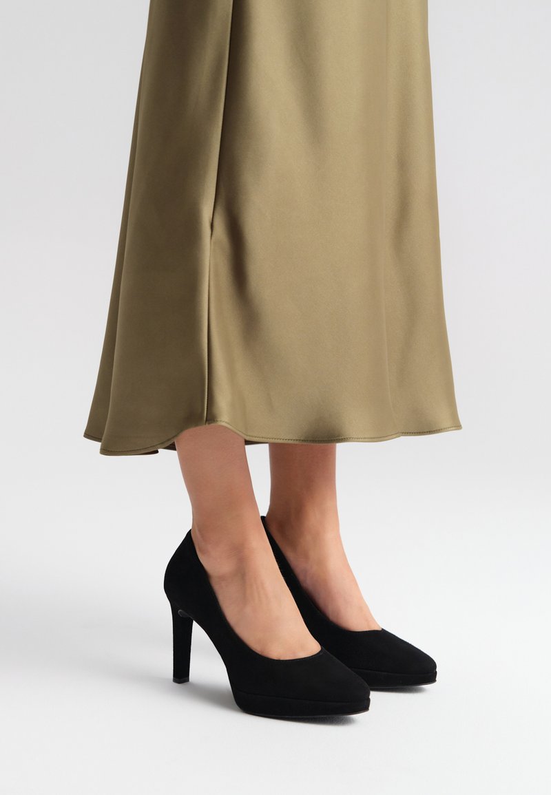 Czarne zamszowe szpilki z okrągłym noskiem i gładką teksturą, zestawione z zwiewną oliwkowozieloną satynową spódnicą.