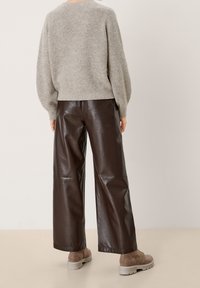 Maglione grigio lavorato a maglia abbinato a pantaloni palazzo in pelle marrone e stivaletti alla caviglia marrone chiaro. Tessuto strutturato con design a vestibilità rilassata.